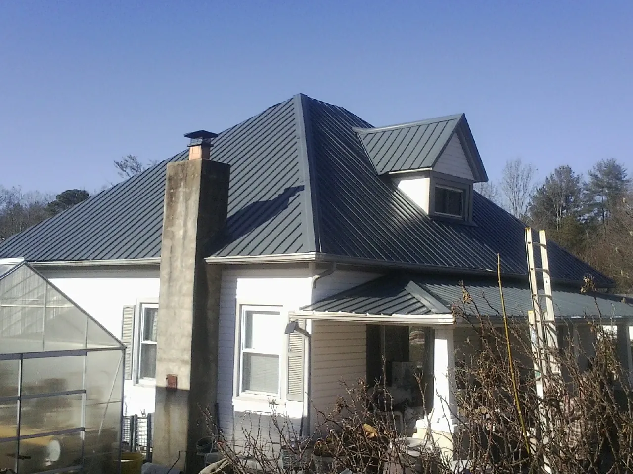 Dark blue standing seam metal roof on a white farmhouse with dormer — Slate & Tile Roof Repair by Roofing Brothers in Keenesburg