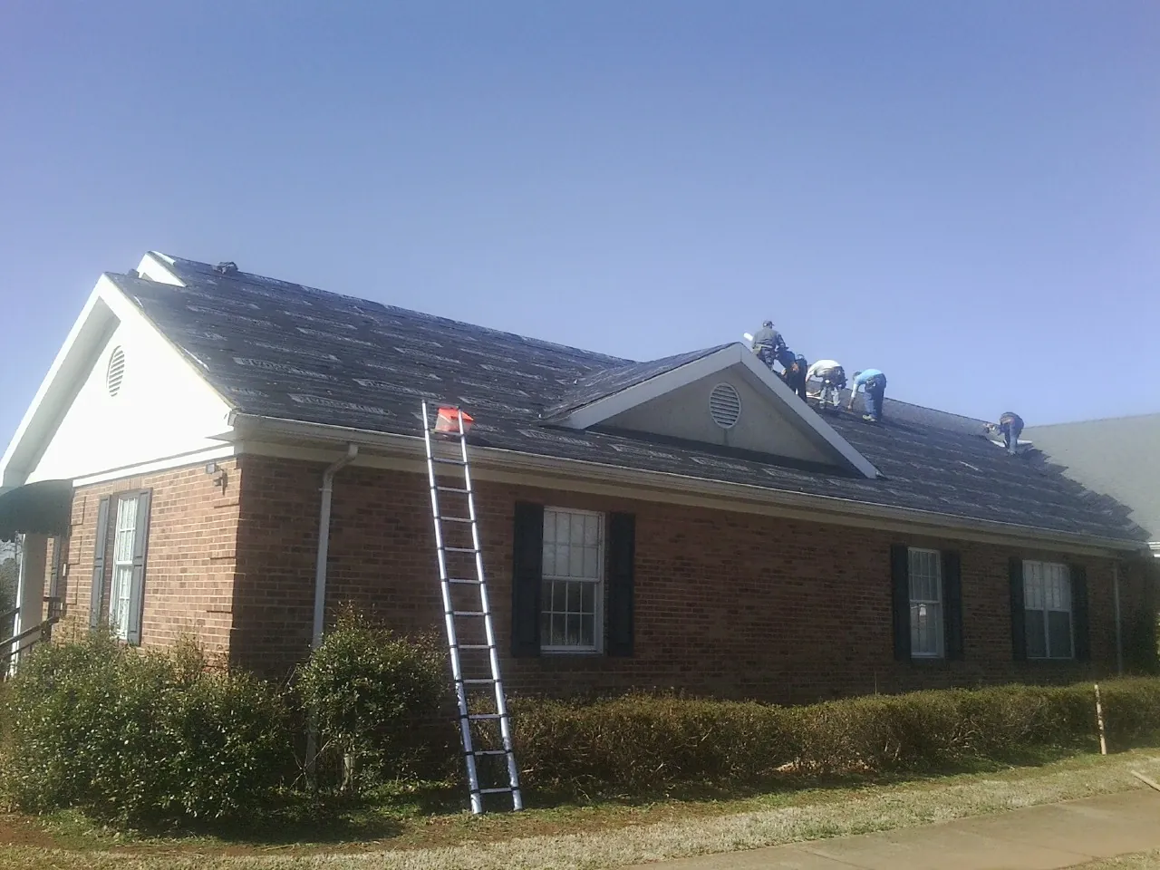 Crew tearing shingles off a brick ranch roof with a ladder set — Emergency Roof Repair work by our crew in Keenesburg