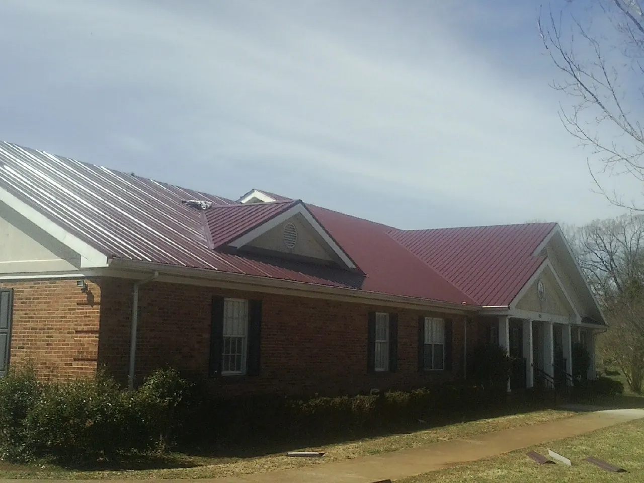 Red metal roof with gabled entries on a long brick building, from a Hail Damage Roof Repair job in Keenesburg