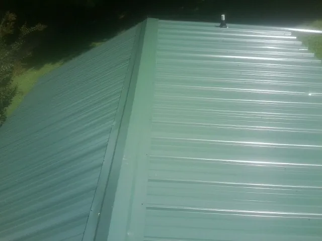 New green metal panels meeting at the ridge of a roof — Flat Roof Repair work by our crew in Keenesburg