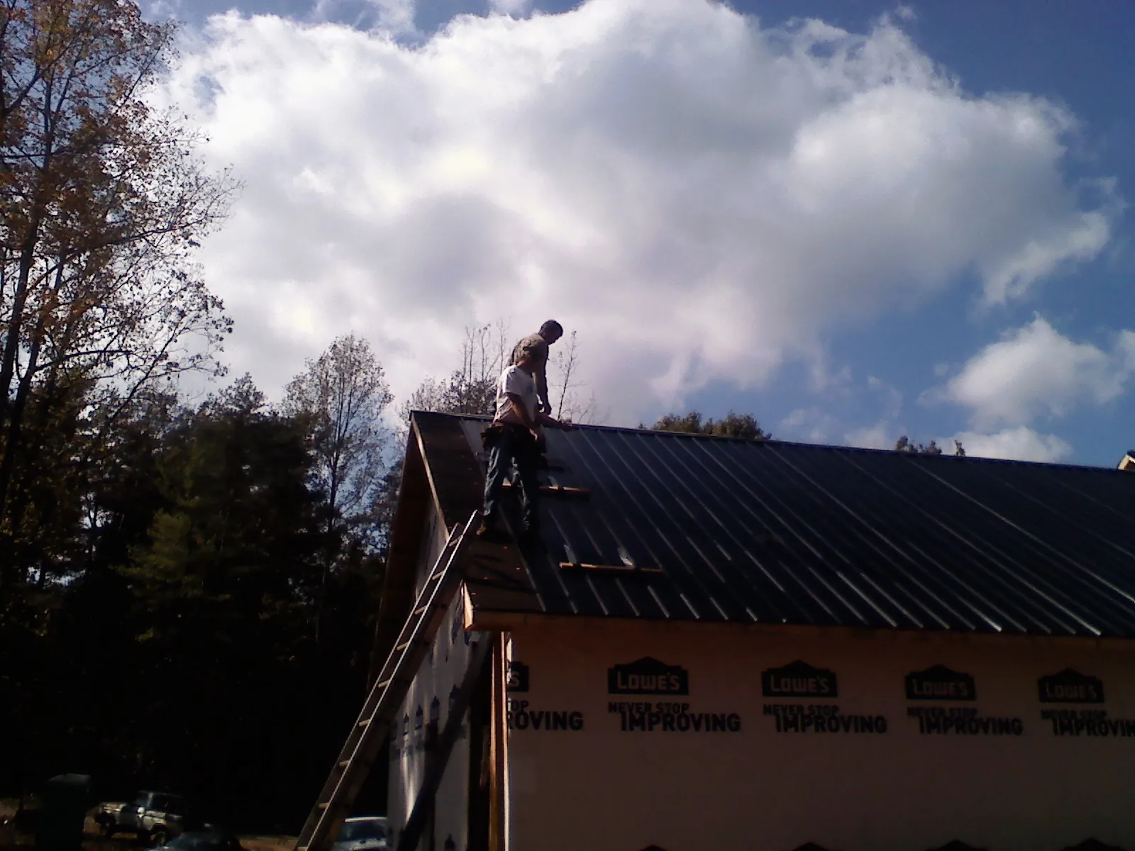 Roofer fastening dark metal panels high against a cloudy sky, from a Roof Inspection job in Keenesburg