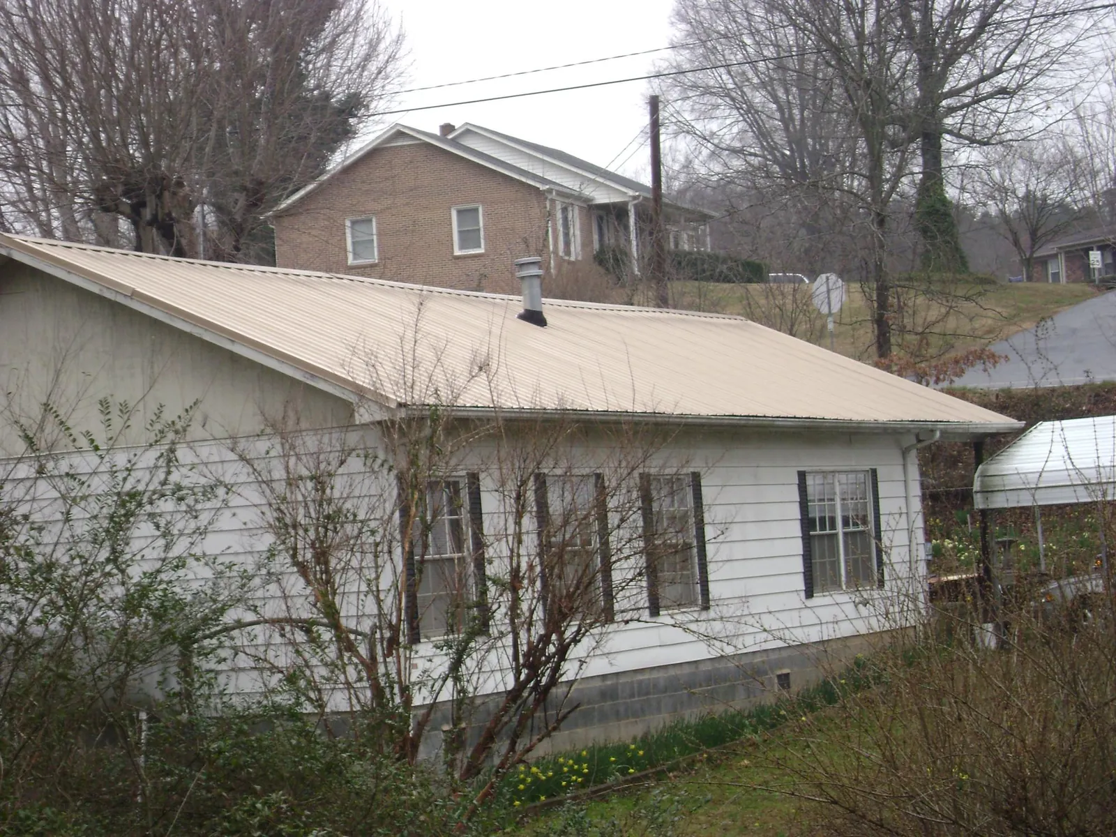 Tan metal roof on a white sided house set into a hillside — Commercial Roofing by Roofing Brothers in Keenesburg