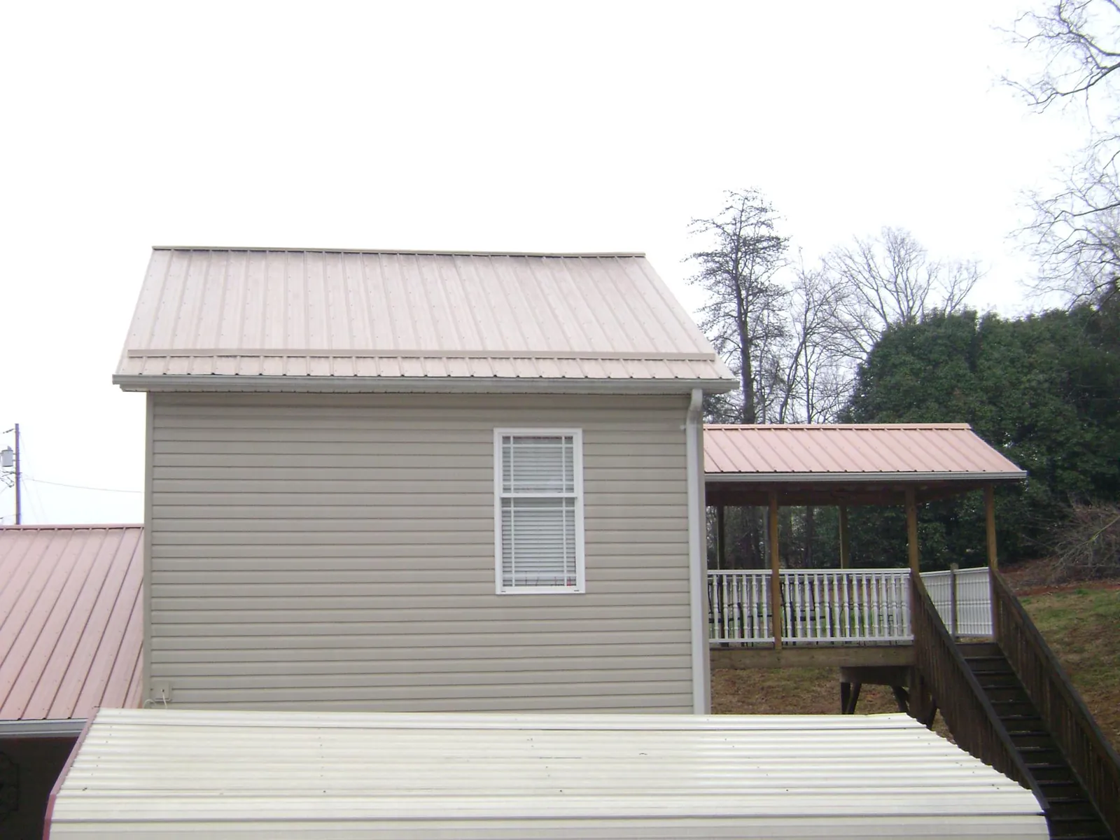 Tan metal roofs on a two story addition and attached porch, from a Roof Replacement job in Keenesburg